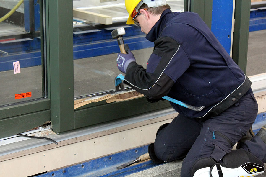 Mann von Testzentrum schlägt mit Werkzeug auf Fensterrahmen ein